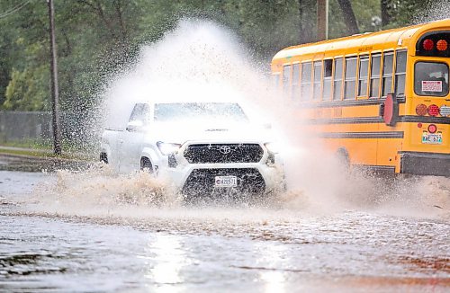 A school bus douses a passing truck with rainwater at a flooded intersection on 13th Street, just in front of the Brandon Fire Station 2 after a morning of rain on Monday. (Matt Goerzen/The Brandon Sun)