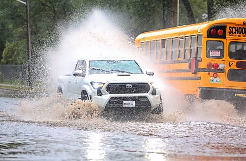 A school bus douses a passing truck with rainwater at a flooded intersection on 13th Street, just in front of the Brandon Fire Station 2 after a morning of rain on Monday. (Matt Goerzen/The Brandon Sun)
