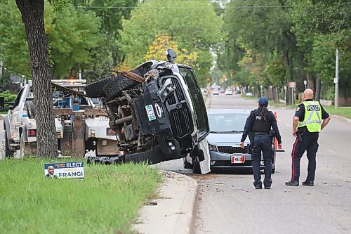 Brandon police officers watch the scene as a crew with Brandon Fire and Emergence Services works with a tow truck operator to pull a flipped black pickup back onto its wheels at the corner of Victoria Avenue and Second Street on Wednesday afternoon. The driver of the truck apparently lost control of the vehicle, hit a tree on the median and flipped shortly after 1 p.m., coming to rest on its side. When it flipped it landed on the hood of a four-door sedan that was driving behind. The driver of the truck had to be pulled from the vehicle and was placed on a stretcher before being taken to hospital. (Matt Goerzen/The Brandon Sun)