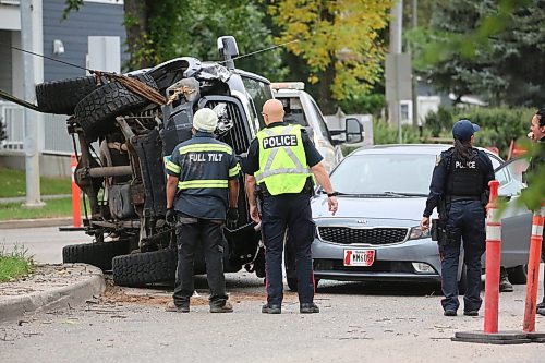 Brandon police officers watch the scene as a crew with Brandon Fire and Emergence Services works with a tow truck operator to pull a flipped black pickup back onto its wheels at the corner of Victoria Avenue and Second Street on Wednesday afternoon. The driver of the truck apparently lost control of the vehicle, hit a tree on the median and flipped shortly after 1 p.m., coming to rest on its side. When it flipped it landed on the hood of a four-door sedan that was driving behind. The driver of the truck had to be pulled from the vehicle and was placed on a stretcher before being taken to hospital. (Matt Goerzen/The Brandon Sun)