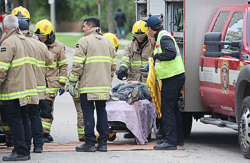 A crew with Brandon Fire and Emergence Services speak with the driver of a black truck who has been placed on a stretcher at the corner of Victoria Avenue and Second street after the eastbound vehicle he was in hit a tree on the median and flipped shortly after 1 p.m. on Wednesday, coming to rest on its side, and balanced on the hood of a four-door sedan that was driving behind.  (Matt Goerzen/The Brandon Sun)