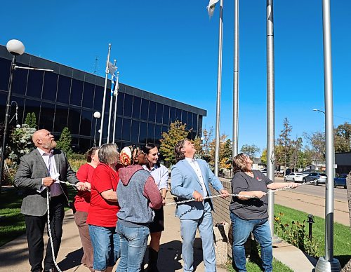 Coun. Tyson Tame (Ward 10), Mayor Jeff Fawcett, Cynamon Mychasiw accompanied by United Way West Central Manitoba employees raising the flag at City Hall on Monday. (Rylee Gerrard/The Brandon Sun)