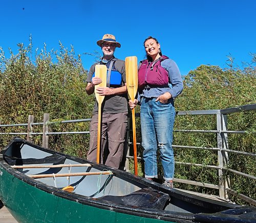 Brandon Riverbank Discovery Centre executive director Dean Hammond and community co-ordinator Ingrid Gatin stand beside a canoe on a dock that overlooks the Assiniboine River. (Rylee Gerrard/The Brandon Sun)