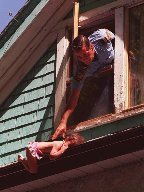 Winnipeg Fire Dept. Captain Marcel Lafond  leans through  third story window to rescue a two and a half year old girl who managed to make her way out onto the eves trough where she became lodged. Due to a misdirected 911 call the child was stuck out  on the ledge for over20 miniutes before the fire dept.  was brought to the scene by a neighbor.The fire captain and another fireman broke down the  locked door and rushed up the the 3rd floor, where Cpt. Marcel LaFond  reached out to the childs and pulled her in without injury.  One year later this child died in a second fire , started by children playing with matches . see Bill Redekop story  re: inquest - Ken Gigliotti Winnipeg Free Pree CP photo July 30 1997.